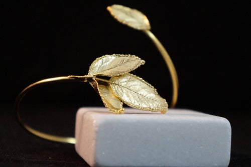 Gold leaf-shaped hair accessory on a gray stand with a black background